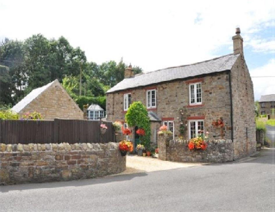 an old stone house with flowers in front of it at Hadrians Wall Cottage, Greenhead in Greenhead