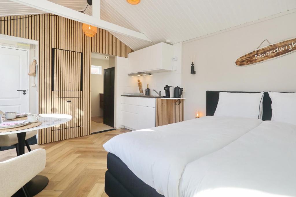 a bedroom with a large white bed and a kitchen at Huisje bij Zee (gratis parkeren) in Noordwijk aan Zee
