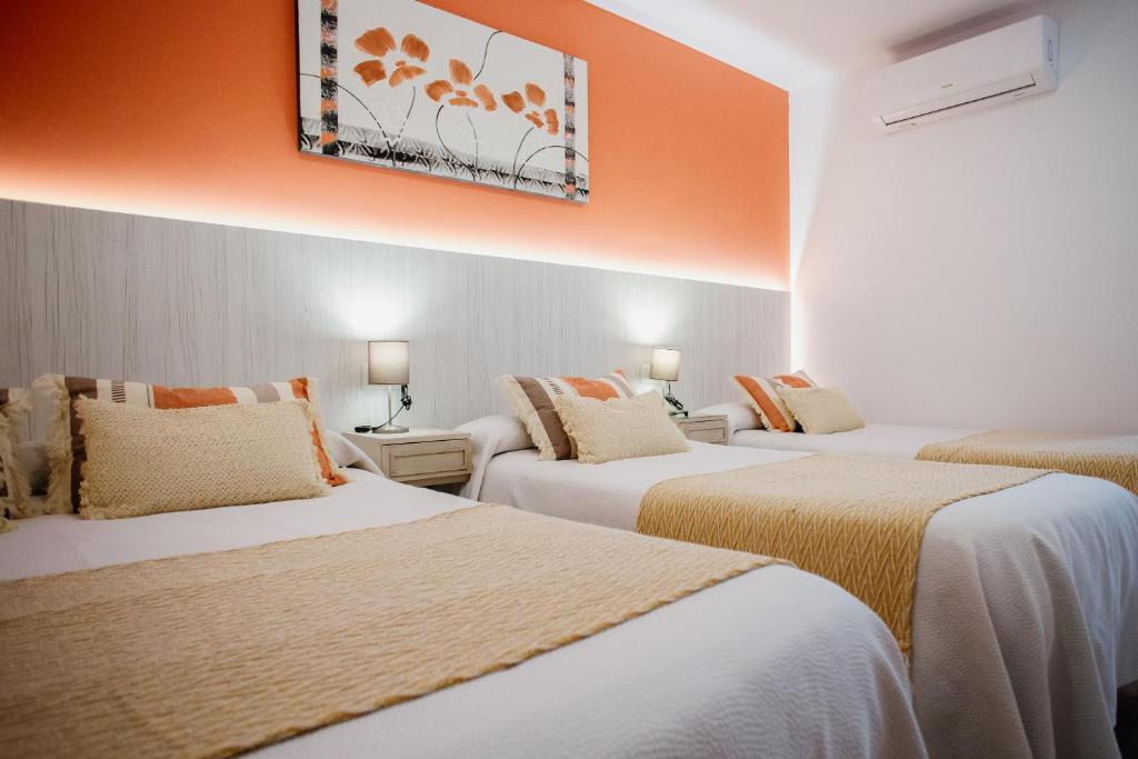 three beds in a hotel room with an orange wall at Pensión mastil 16. P2 in Málaga