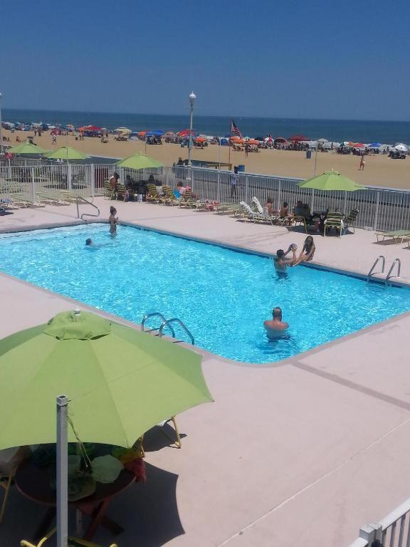 ein Swimmingpool mit einem grünen Sonnenschirm und Menschen darin in der Unterkunft Fish Tales Boardwalk Inn &amp; Ocean Mecca Motel in Ocean City