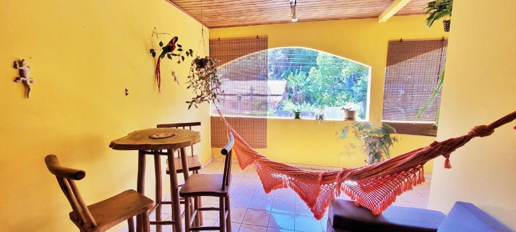 eine Hängematte in einem Zimmer mit einem Tisch und einem Fenster in der Unterkunft Casa Sapucaia - Praia in Santa Cruz Cabrália