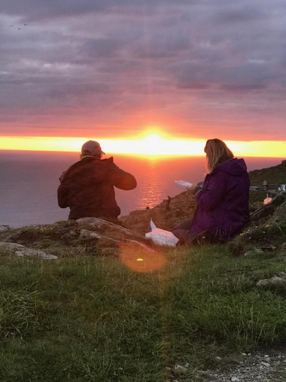 Duas pessoas sentadas numa colina a ver o pôr-do-sol. em The Little Garden Hideaway with Stunning Sea Views and Garden em Holyhead