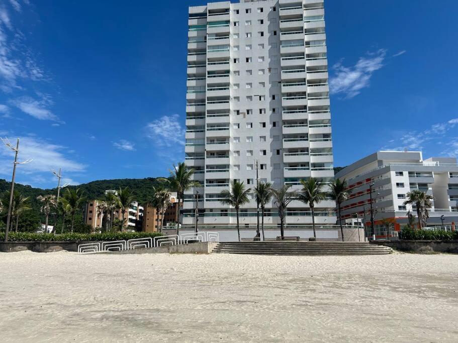 un grand bâtiment avec des bancs et des palmiers devant lui dans l'établissement Pé na areia, Solemar Praia grande, à Praia Grande