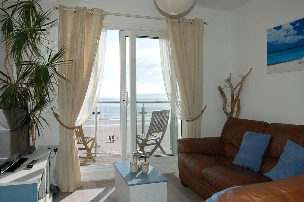 a living room with a couch and a view of the ocean at Chwerthin Y Mor Beach House in Tywyn