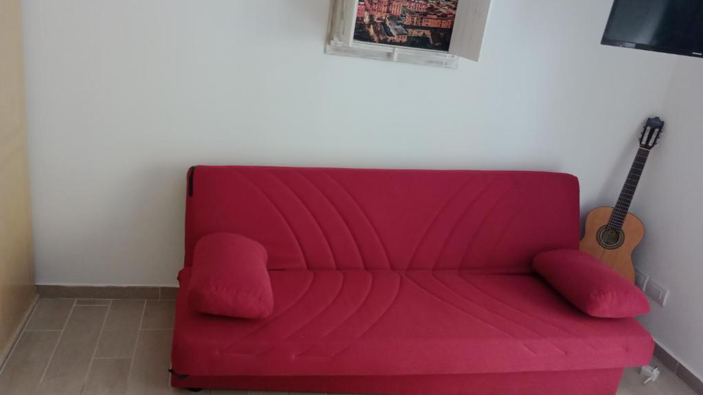 un divano rosso in una stanza con chitarra di Monolocale al centro di Napoli A' fenestrella a Napoli