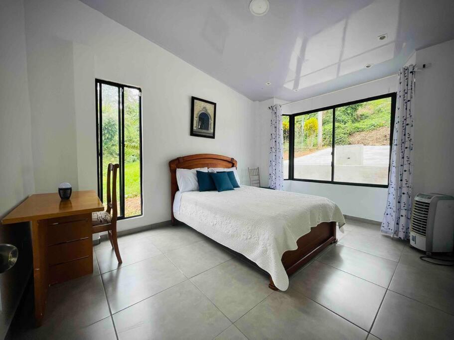 a bedroom with a bed and a desk and two windows at Chega de Saudade in Puerto Quito
