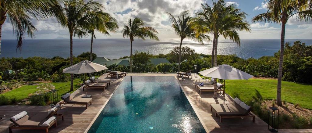 una piscina con sillas y sombrillas y el océano en Luxury Vacation Villa 3, en Gustavia