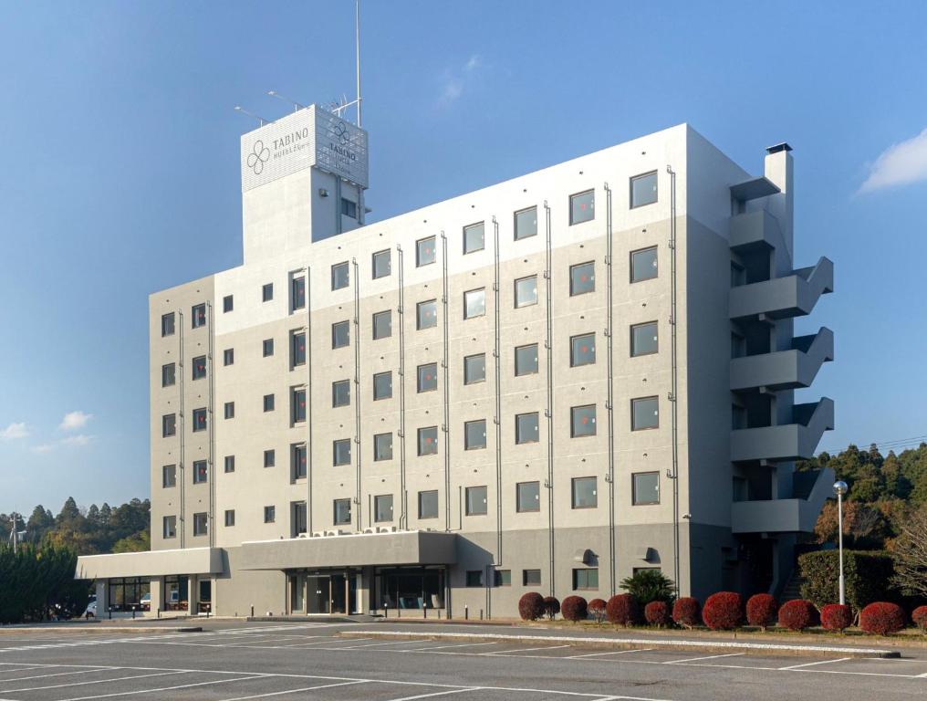 un grand bâtiment blanc avec un parking en face de celui-ci dans l'établissement Tabino Hotel EXpress Narita, à Narita