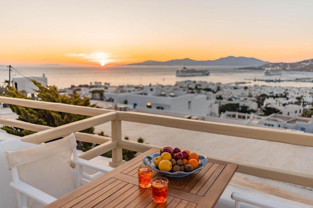 a bowl of fruit on a table on a balcony with the sunset at Pelican Hotel in Mikonos