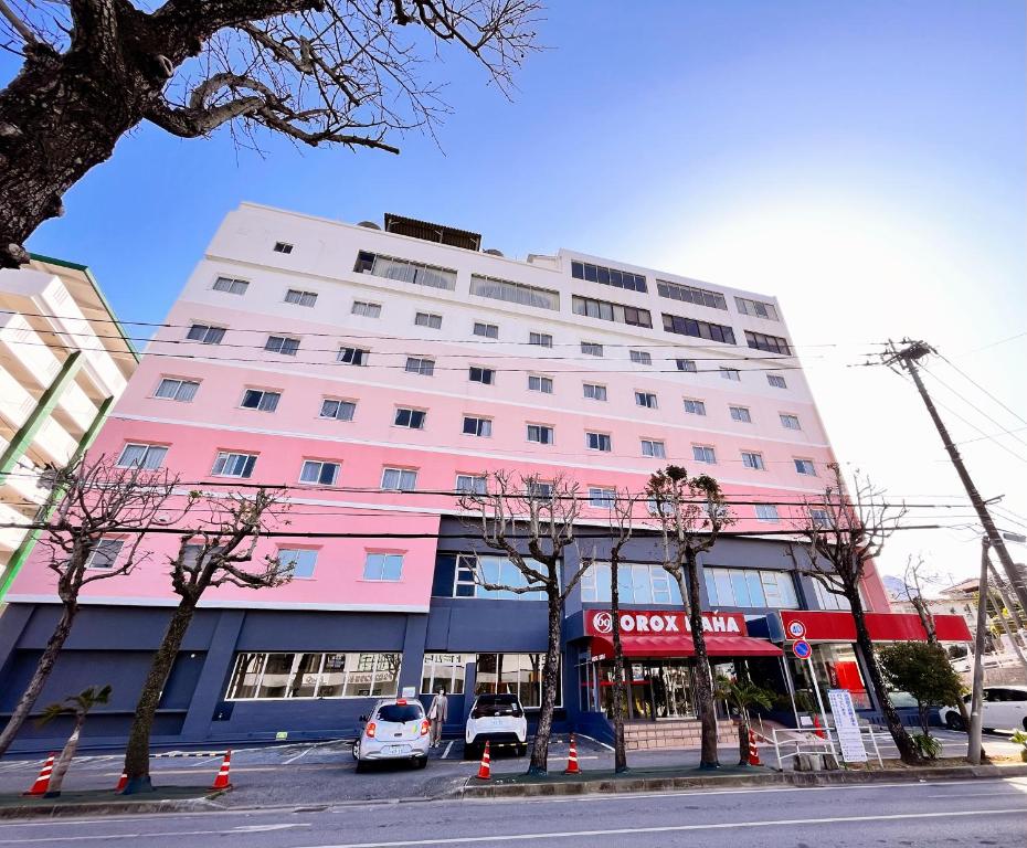różowy budynek z samochodami zaparkowanymi przed nim w obiekcie Hotel Orox w mieście Naha