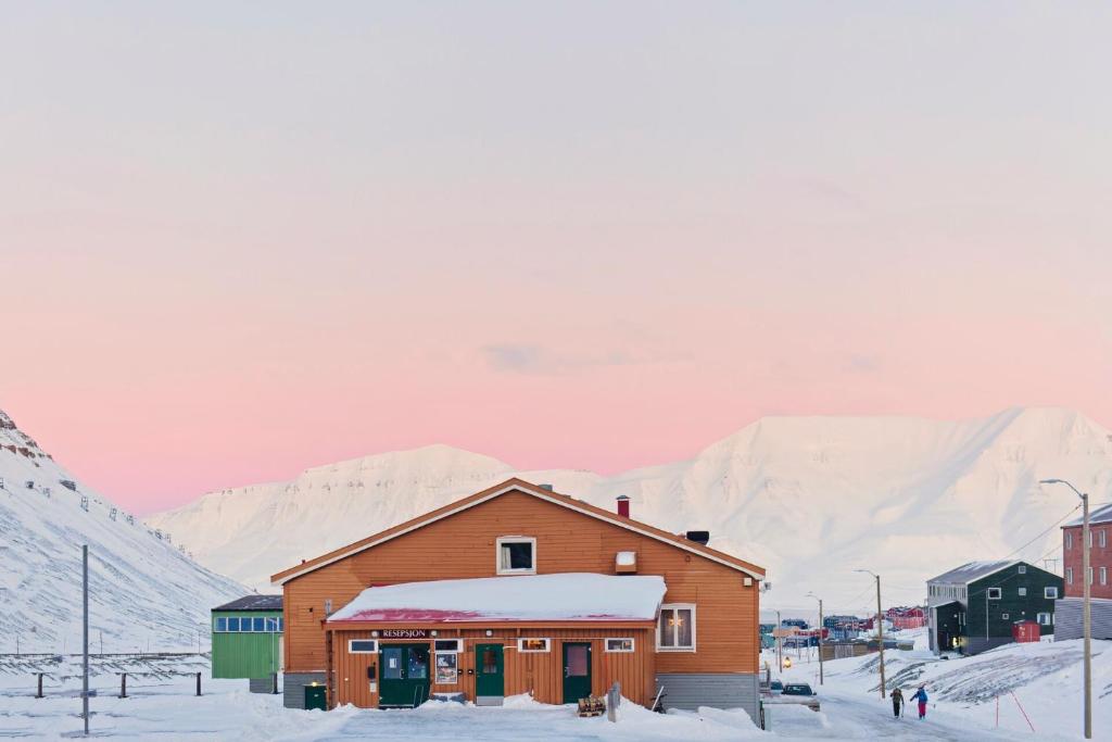 a building in the snow with mountains in the background at Coal Miners’ Cabins in Longyearbyen