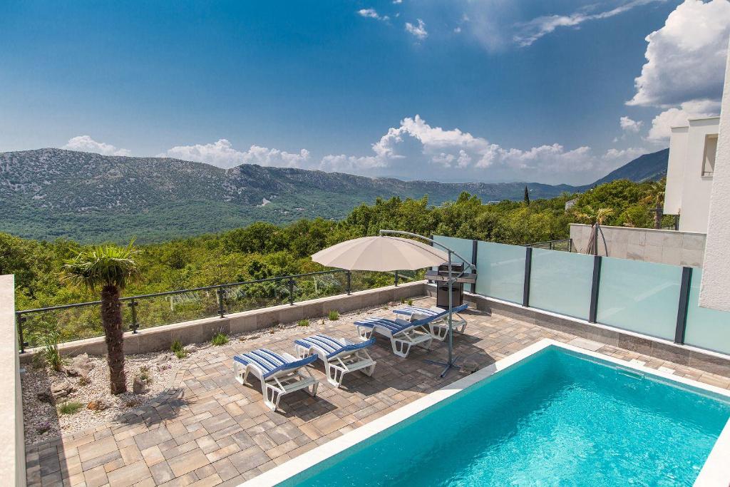 a villa with a swimming pool and a patio with chairs and an umbrella at Exklusive Privatvilla in wunderbarer Natur in Antovo