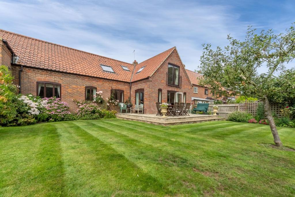 uma casa de tijolos com um grande quintal em frente em Saxon Shore Cottage em Burnham Deepdale