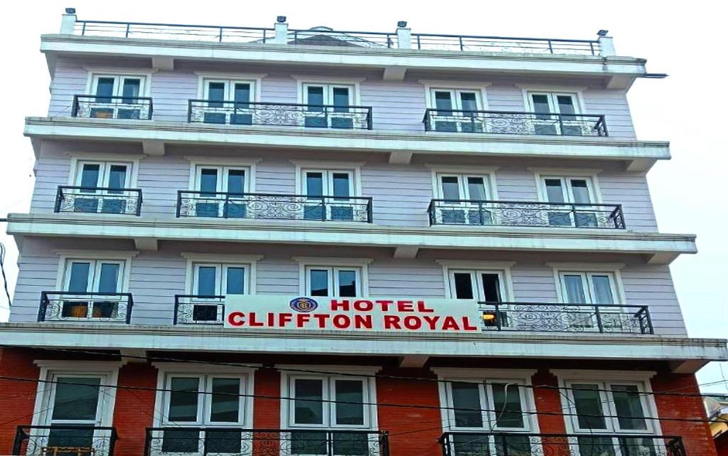 un grande hotel bianco con un cartello di fronte di HOTEL CLIFFTON ROYALS a Darjeeling