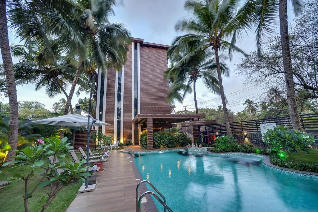 a swimming pool in front of a building with palm trees at Cygnett Inn Celestiial Goa in Candolim