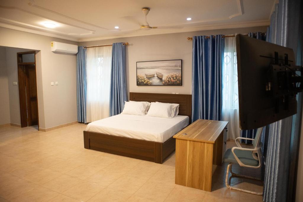a bedroom with a bed with blue curtains and a television at EXECUTIVE MASTER BEDROOM in Accra