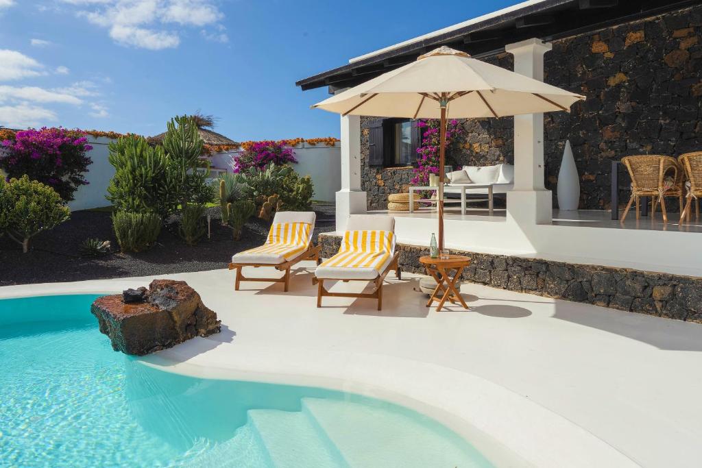 a swimming pool with two chairs and an umbrella at UNIQUE Villas Lajares - Only Adults in Lajares