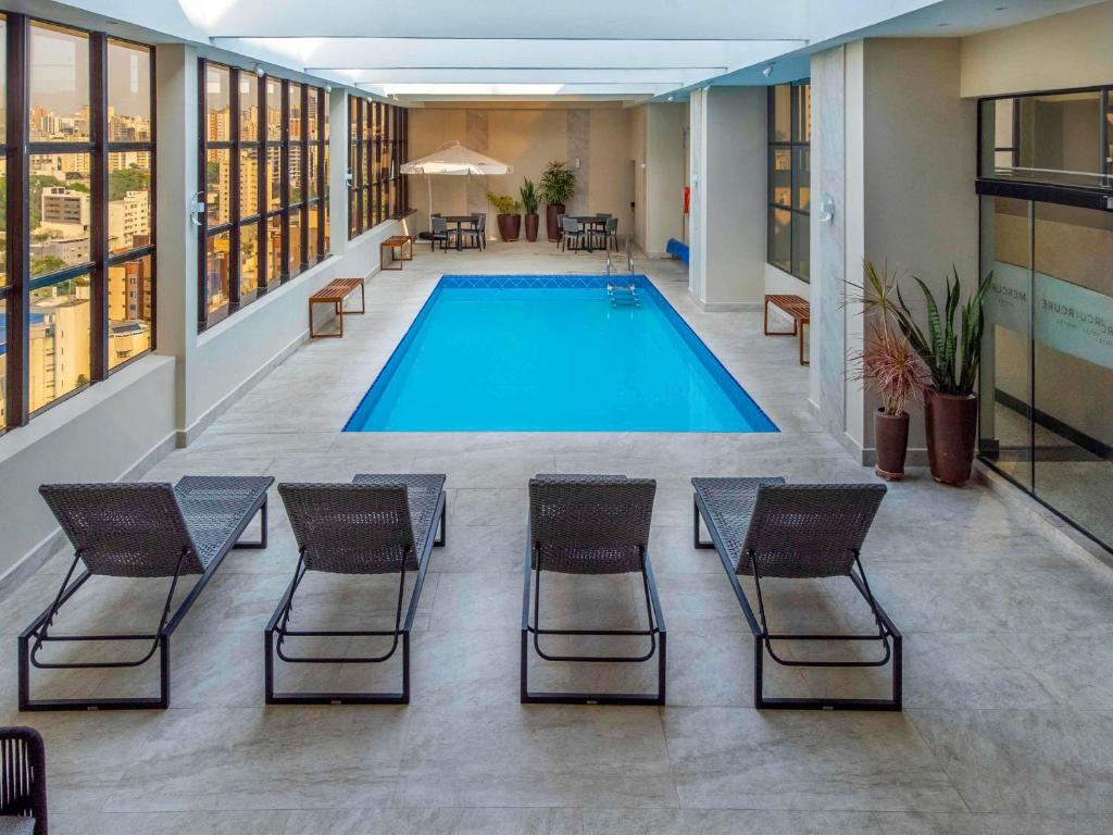 a swimming pool in a building with chairs and a pool at Mercure Curitiba Golden in Curitiba