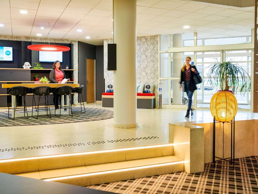 a lobby with people sitting at tables and a counter at Novotel Senart Golf De Greenparc in Saint-Pierre-du-Perray