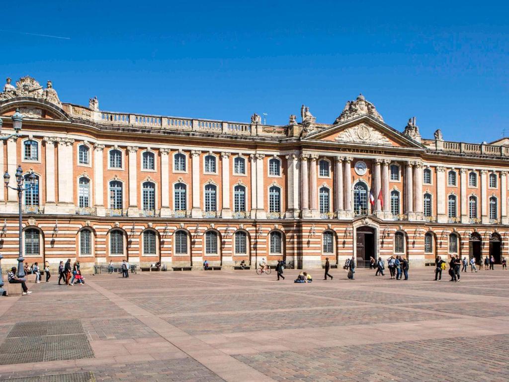 un grand bâtiment avec des personnes qui marchent devant lui dans l'établissement Ibis Styles Toulouse Capitole, à Toulouse