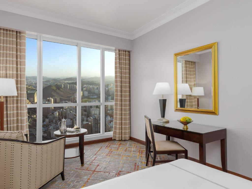 a hotel room with a desk and a large window at Swissotel Al Maqam Makkah in Mecca