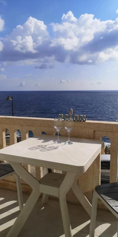 una mesa blanca con 2 copas de vino en el balcón en Excellent views, en Marsalforn