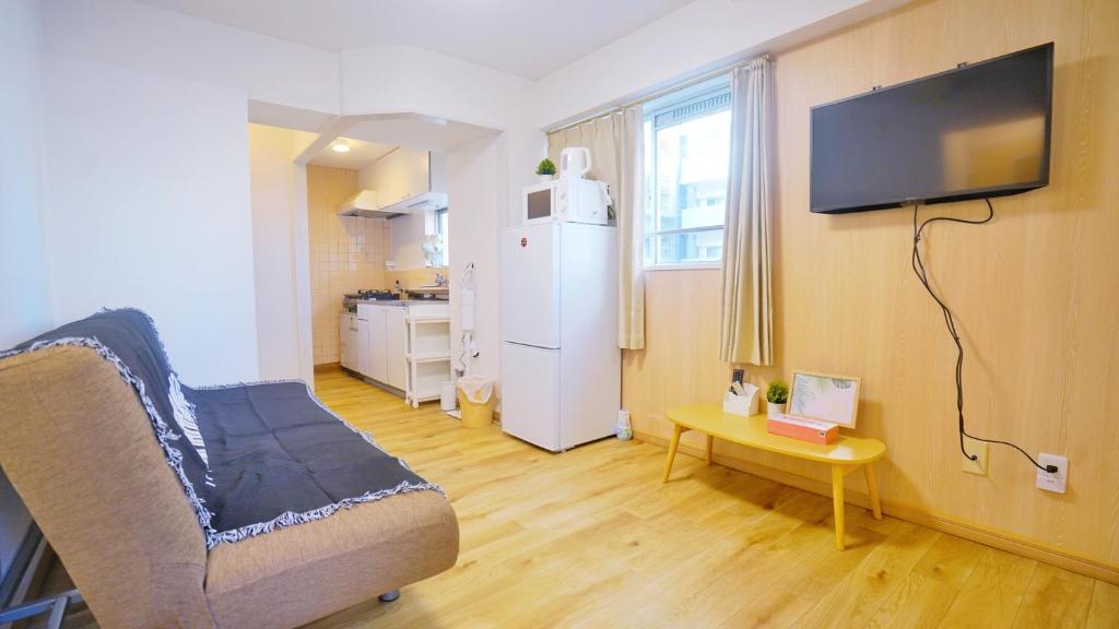 ein Wohnzimmer mit einem Sofa, einem Tisch und einem Kühlschrank in der Unterkunft CowCow Hotel Shinjuku in Tokio