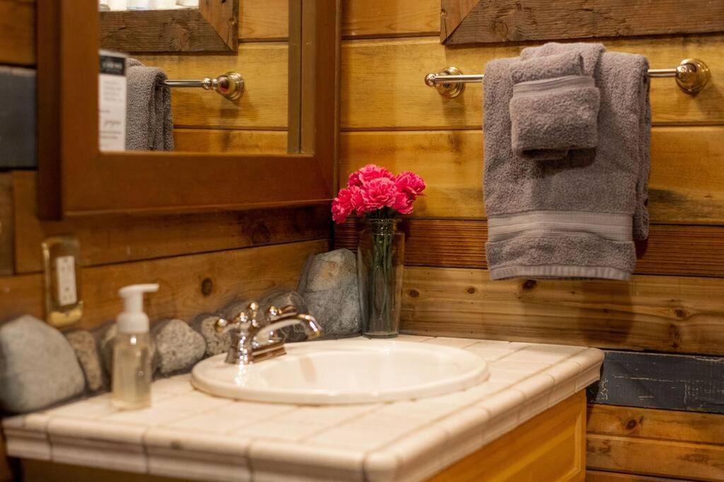 baño con lavabo y jarrón de flores rosas en O'Neill Cabin - a rustic reclaimed retreat, en Index