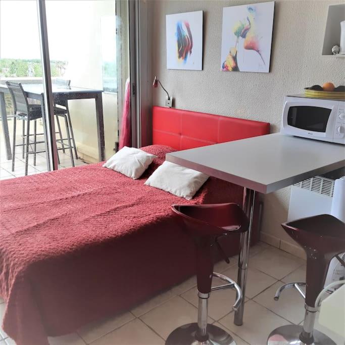 une chambre avec un lit rouge et une table avec des chaises dans l'établissement Studio 17, Héliopolis L au village naturiste, au Cap d'Agde