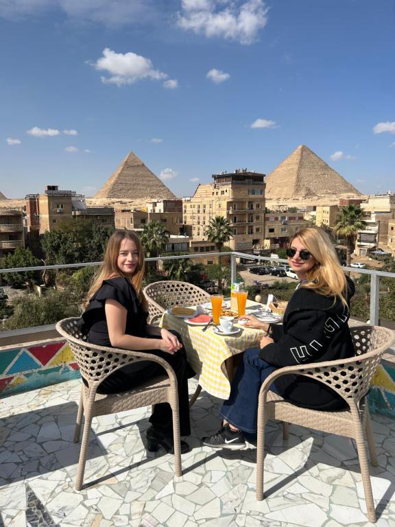 dwie kobiety siedzące przy stole z widokiem na piramidy w obiekcie Matto Pyramids Inn w Kairze