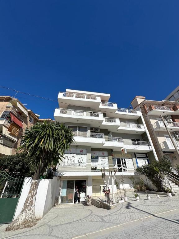 a white building with a palm tree in front of it at Olivias Apartments City Center in Sarandë