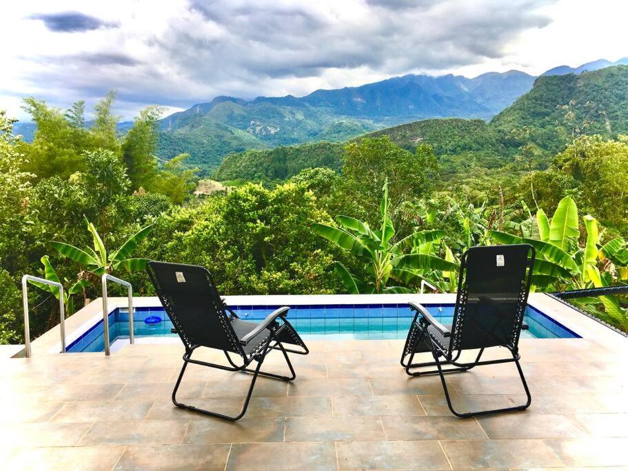 2 chaises assises à côté d'une piscine avec montagnes dans l'établissement FINCA 100x100 PRIVADA- DESCANSO PLACENTERO - Sasaima, à Sasaima