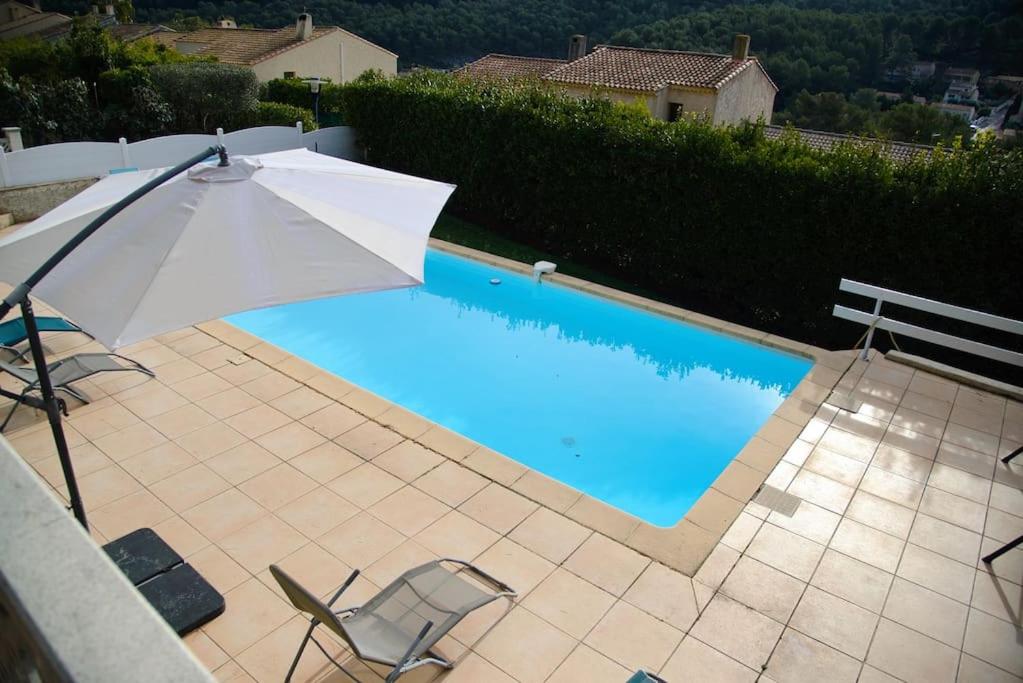 ein Sonnenschirm und Stühle neben einem Pool in der Unterkunft élégante villa avec piscine privée près de cassis in Carnoux