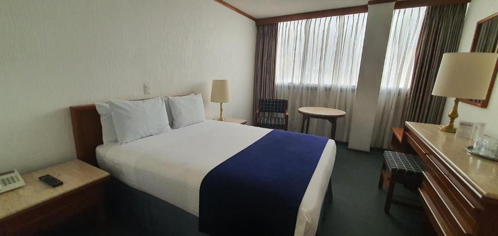 A large-bed room with floor-to-ceiling curtains, a small table, and a dresser desk.