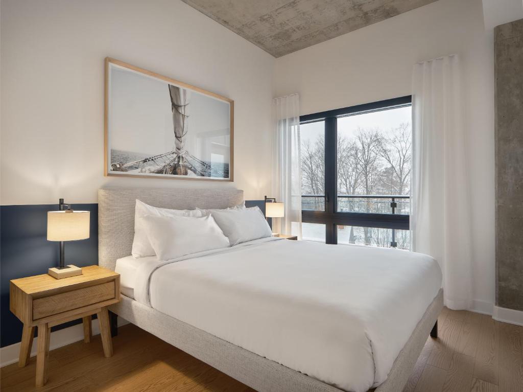 a white bedroom with a large bed and a window at Hôtel - Expérience - Quartier Des Marinas in Magog-Orford