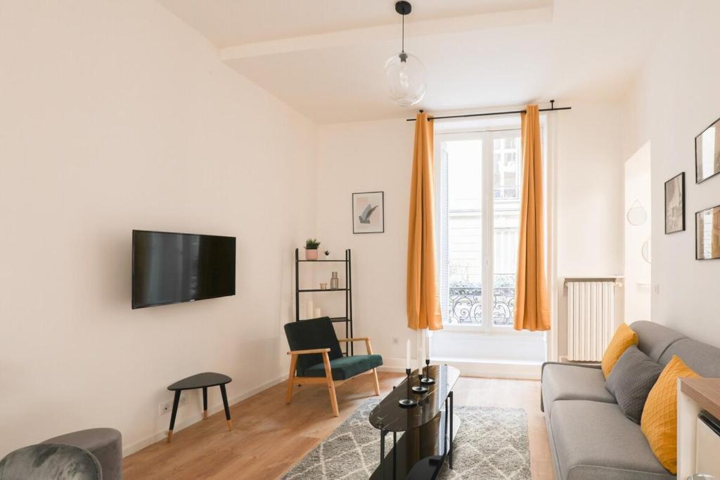 a living room with a couch and a tv on a wall at Charmant appartement proche Opéra Garnier - 4p in Paris