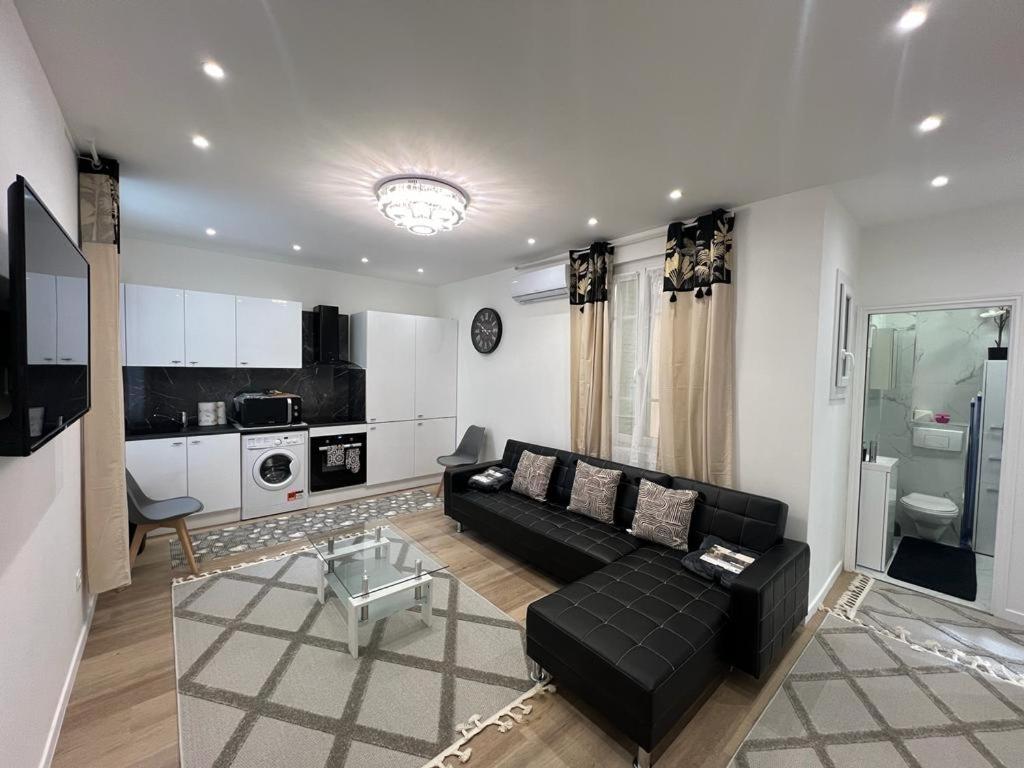 a living room with a black couch and a kitchen at Appartement T2 in Nice