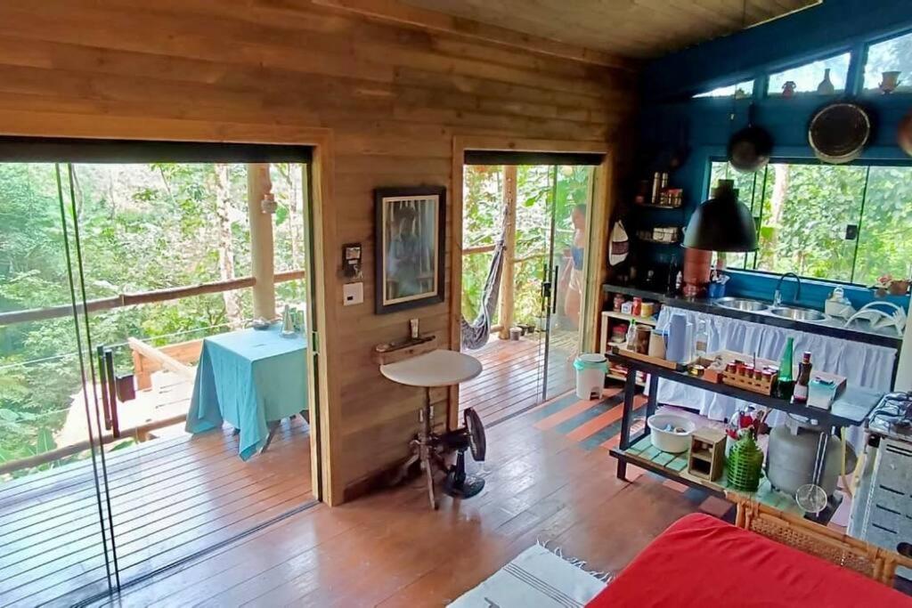 een woonkamer met een houten vloer en een keuken bij Eco Cabana a 150 metros da praia e centrinho in Paraty