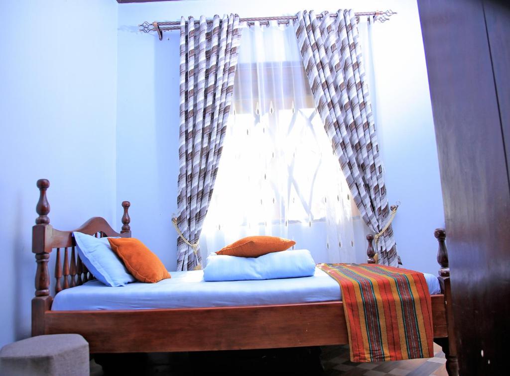a bed with orange pillows in front of a window at Heavenly Royalz Farm Fortportal in Njara