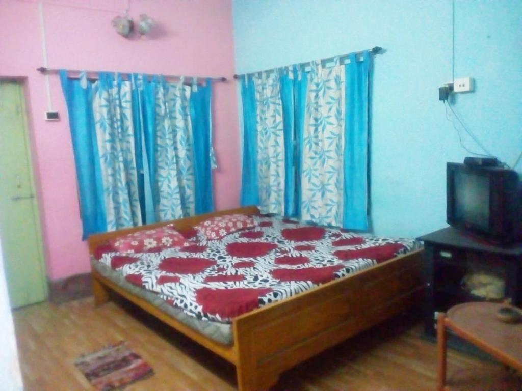 a bedroom with a bed with blue curtains and a tv at Sonarbangla in Digha