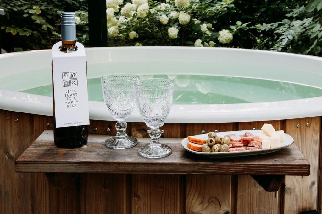 una botella de vino y copas en una mesa junto a la bañera en Welness Bungalow midden in het bos, en Rheezerveen