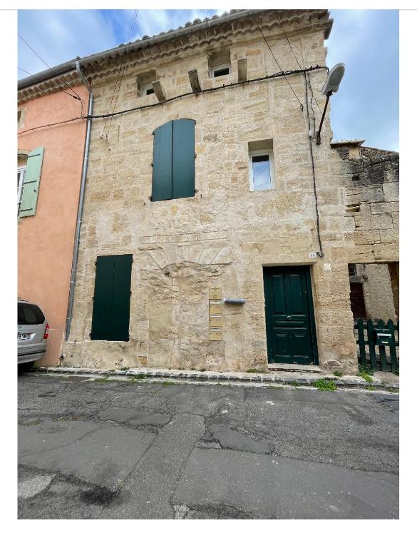 - un vieux bâtiment en pierre avec des portes et des fenêtres vertes dans l'établissement Bel Appartement, à Saint-Thibéry