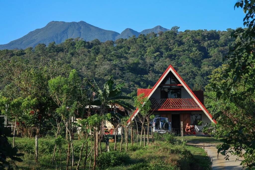 a house with a red roof with mountains in the background at Cabaña Las Colinas in Bijagua