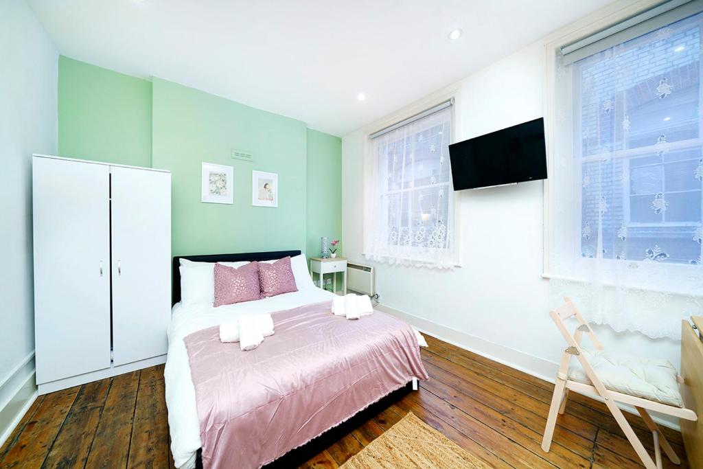 Schlafzimmer mit einem Bett mit rosa Bettwäsche und einem TV in der Unterkunft Brewer Street Central Apartments in London