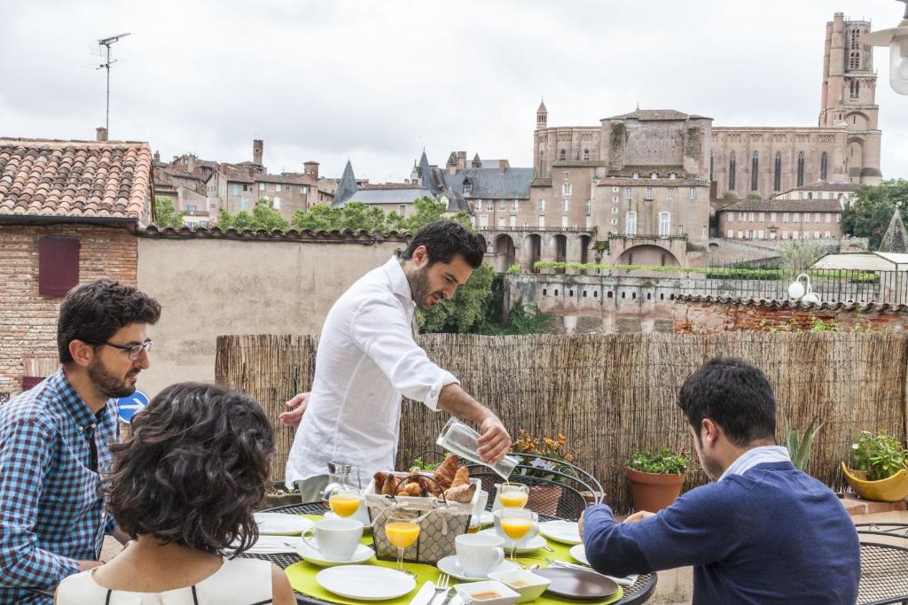 een man die eten serveert aan een tafel met een groep mensen bij Villa Caroline - Chambres d'Hôtes in Albi