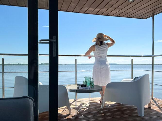 a woman in a white dress standing on a balcony at Comfortable house on the water for 3 people in Łazy