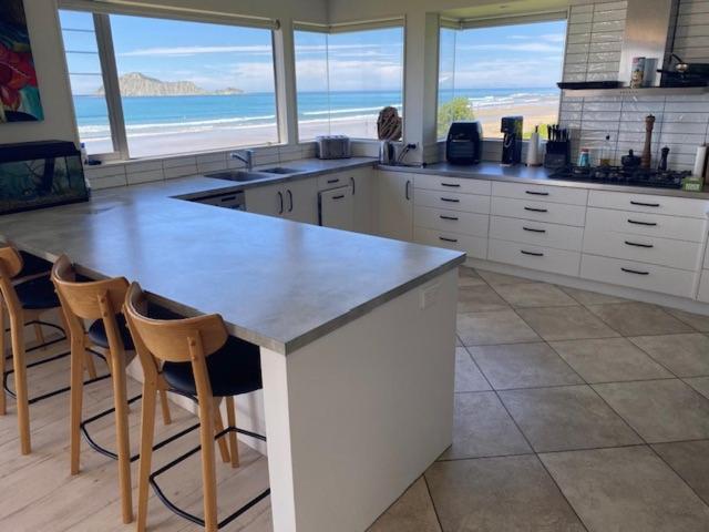 a kitchen with a large counter with chairs and the ocean at Ultimate Beach Front in Waimarama