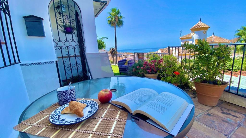 einen Glastisch mit einem offenen Buch und einem Apfel und einem Teller Essen in der Unterkunft Apartamento en La Noria Nerja by At Home Costa del in Nerja