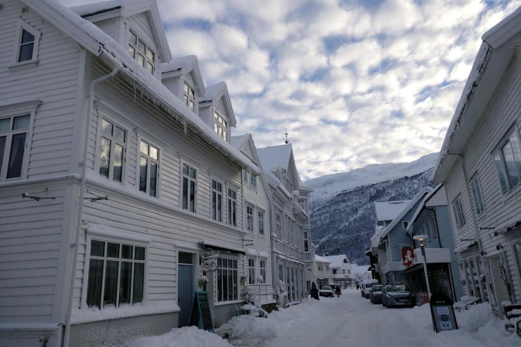 eine verschneite Straße in einer Stadt mit Gebäuden und Bergen in der Unterkunft Sjarmerande hus i Eidsgata in Nordfjordeid