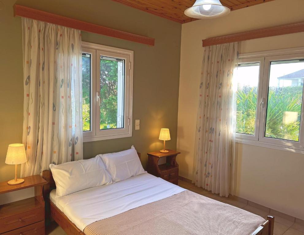 a bedroom with a bed with white sheets and two windows at Orfanos Houses No2 in Koroni